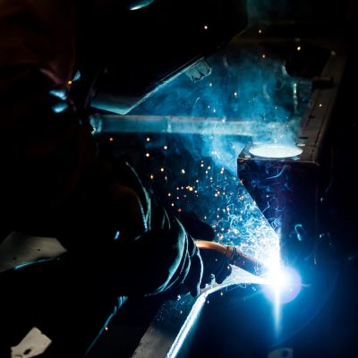 冬瓜机械工业内容主笔罗工站在加工车间金属护栏旁，手拿记录本对照设备铭牌逐项核对参数，背景是暖色厂房灯光